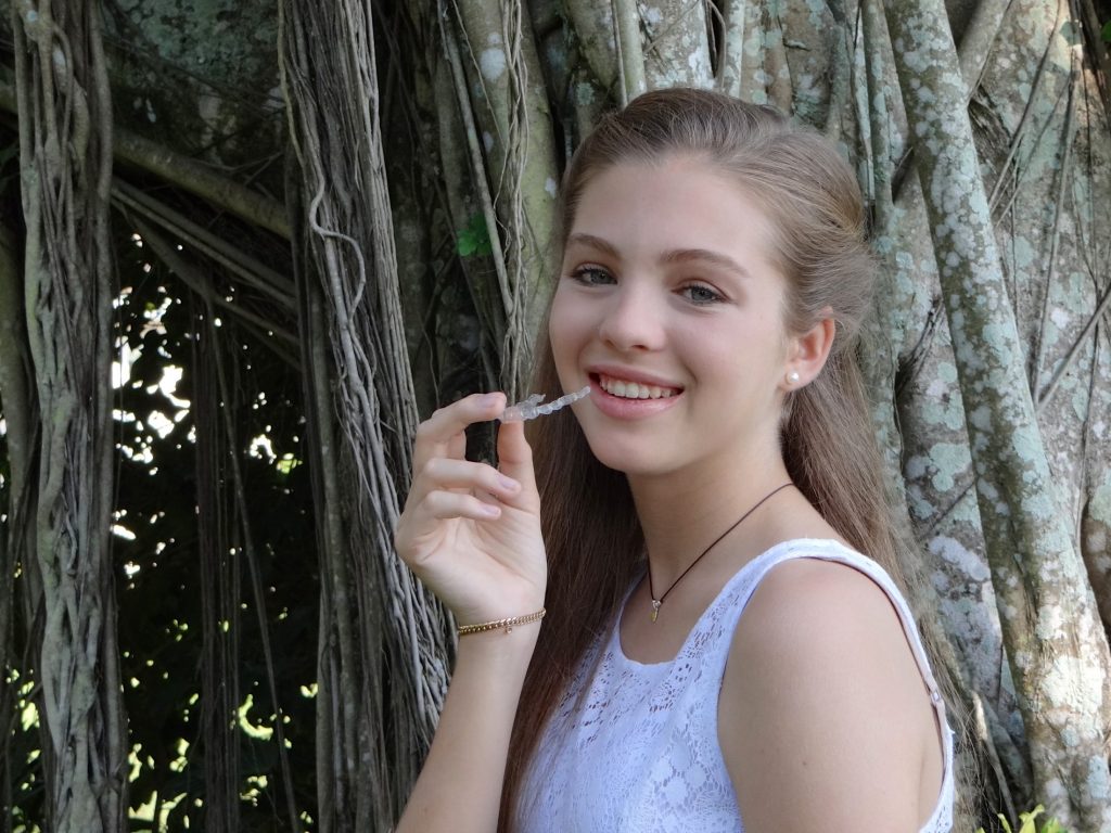 A girl smiling with Invisalign in her fingers